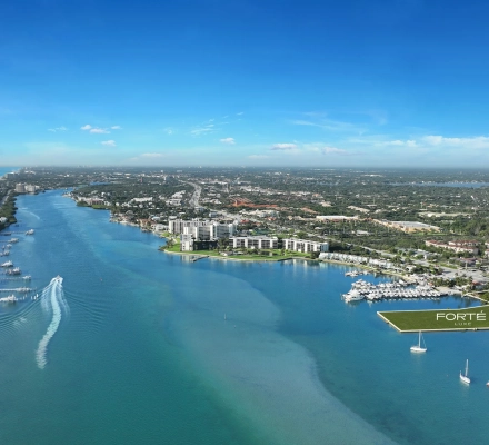 Aerial drone photo of the Intracoastal Waterway in Jupiter with a boat wake, private docks and beachfront condos on the left, and a green lot outlined in white and labeled Fort&eacute; Luxe beside a marina on the right.