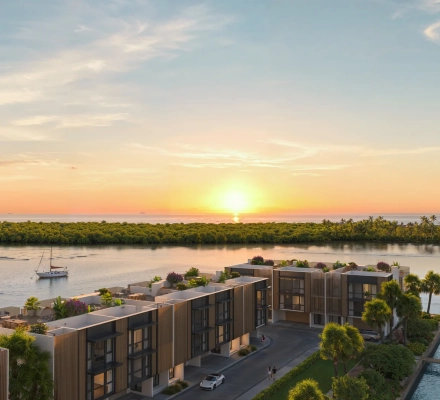Rendering of three-story modern townhome-style residences with wood slat facades and planted rooftop terraces along a private drive, beside calm water with a sailboat, a paddleboarder and a dock, under a sunrise sky.