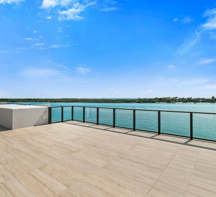 Expansive tiled terrace with glass railing overlooking turquoise water and mangroves.